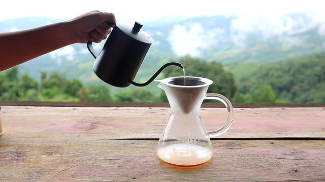 Glass cup with drip coffee  from kettle on wooden table in the nature background ,coffee time in the morning time with mountain view and natural green view feeling chill and relax.