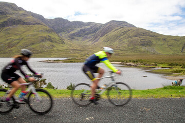 Blurred cyclists on the road R335, on the lakeside of Doo Lough, County Mayo, Ireland