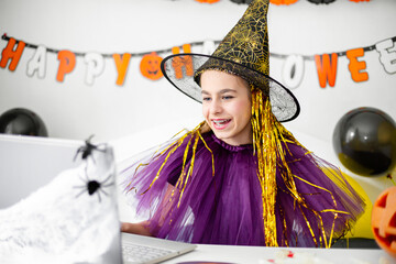 Halloween holiday concept. Cute little girl in witch costume sitting behind a table in Halloween theme decorated room.