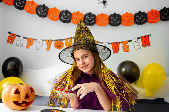 Halloween holiday concept. Cute little girl in witch costume sitting behind a table in Halloween theme decorated room.