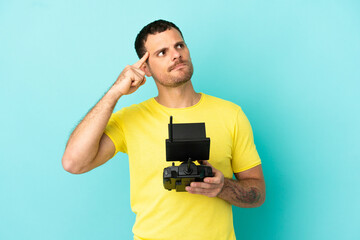 Brazilian man holding a drone remote control over isolated blue background having doubts and thinking