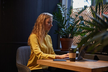 young well dressed cauasian woman sitting at table, working on laptop. beautiful lady typing on computer keyboard at cafe. modern communication technology, distant work, remote job, freelance