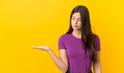 Teenager Brazilian girl over isolated yellow background holding copyspace with doubts