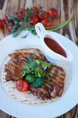 A piece of fried meat lies on a white plate. Decorated with vegetables and herbs. There is a red sauce nearby. The concept of recipes from the restaurant