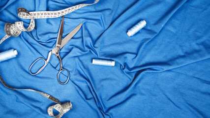 Top view of blue coloured fabrics with thread spools, tape measure, tailoring scissors