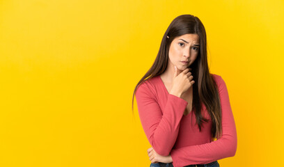 Teenager Brazilian girl over isolated yellow background having doubts