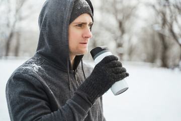 Man athlete drinking from the thermal mug during snowy winter day
