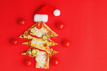 Delicious vegetarian Christmas tree pizza with tomatoes, vegetables and cheese on red background. Creative, funny food concept for kids. Top view, flat lay. Copy space. 