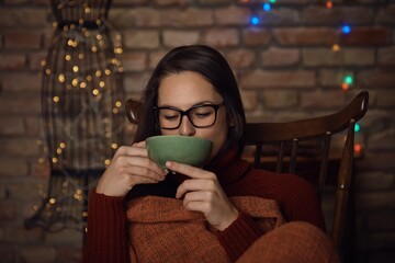Young woman sitting in rocking-chair at home, drinking hot tea at wintertime.