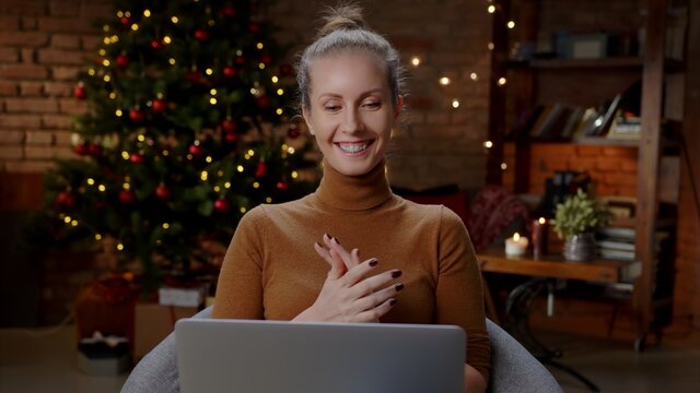 Young woman at home in Christmas time talking on video chat online on laptop computer. Happy and smiling, christmas tree in background.