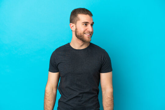 Young handsome caucasian man isolated on blue background looking to the side and smiling