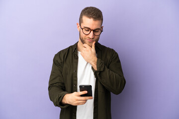 Young handsome caucasian man isolated on purple background thinking and sending a message