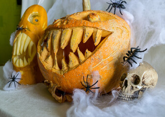 carved pumpkin with a scary smile, spiders, skull, white spider web background, decoration and...
