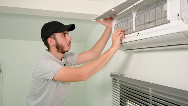 handsome young man electrician cleaning air filter on an indoor unit of air conditioning system in client house