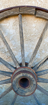 vintage old rusty wooden wagon wheel standing against a old west stucco wall