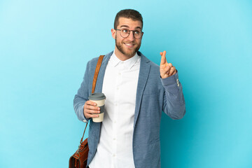 Young caucasian businessman isolated on blue background with fingers crossing and wishing the best