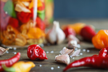Habanero pepper with variety of other spicy peppers and garlic cloves in front of a mason jar of fermenting hot sauce. Selective focus with blurred background and foreground.