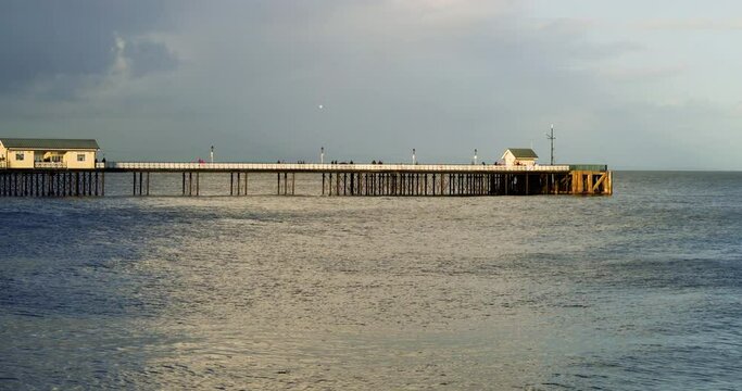 Penarth Pier at high tide: Golden hour at this Welsh tourist attraction and the last rays of setting sunlight hits the pier at dusk. The sea is calm and in the foreground and creates a tranquil scene.