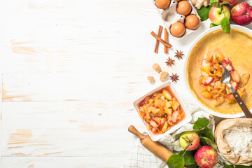 Apple pie cooking. Homemade cooking. Pie dough in a baking dish, apple filling and ingredients on white wooden table. Top view with space for design.