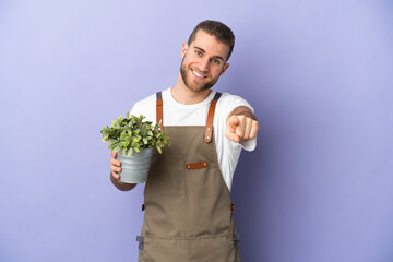 Gardener caucasian man holding a plant isolated on yellow background pointing front with happy expression