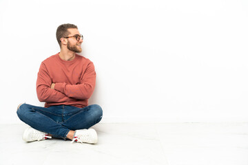 Young handsome man sitting on the floor with arms crossed and happy