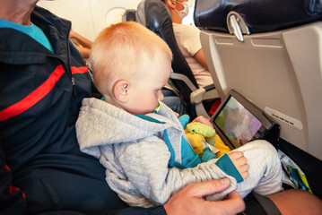 Little child with tablet computer on the lap sitting in the plane.