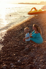 Fototapeta na wymiar A mother with a child on the seashore watching the sunset. Rocky beach, vacation vacation.
