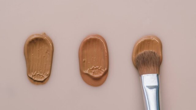 Smearing foundation tones on beige background. Brown cream texture close-up, using brush. Makeup and beauty products concept, cosmetics, eyeshadow palette, bronzer or concealer.