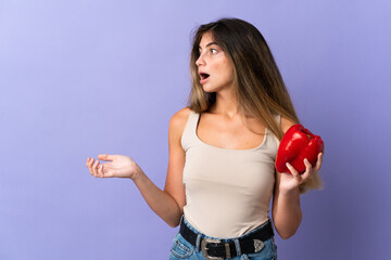 Young woman holding a pepper isolated on purple background with surprise facial expression