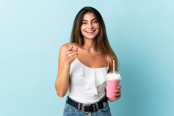 Young woman with strawberry milkshake isolated on blue background surprised and pointing front