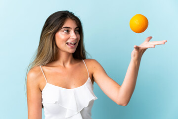 Young caucasian woman isolated on blue background holding an orange