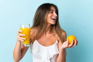 Young caucasian woman isolated on blue background holding an orange and an orange juice