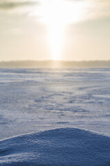 Sun shining above a frozen and snowy lake in Finland in the winter. Focused on the snowbank on foreground. Wintry, sunny and serene landscape at morning.
