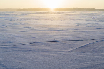 Sun shining above a frozen and snowy lake in Finland in the winter. Wintry, sunny and serene landscape at morning.