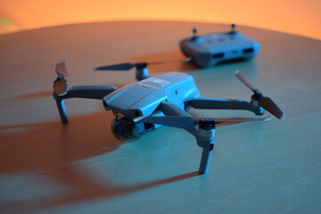 Drone with its background control, on a wooden table, with soft blue and yellow lighting.