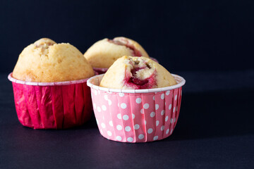 Three muffins with cherry filling on a black background