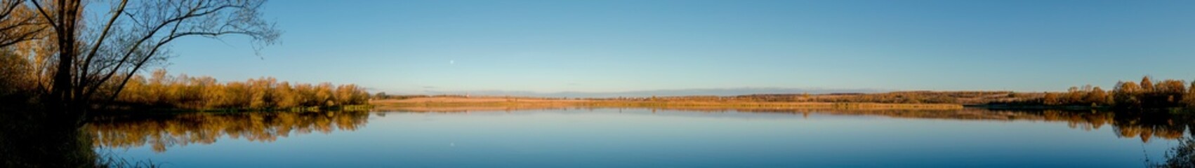 Obraz premium Panorama of autumn lake. Mirror reflection in water, blue sky.