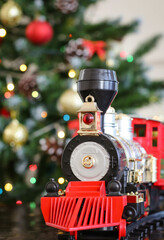 A toy locomotive on the background of a decorated Christmas tree with bokeh from a garland. Christmas and New Year celebration concept, background.