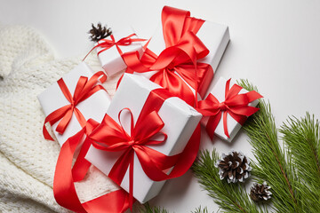 Christmas gift boxes with red ribbon and knitted sweater with green pine tree branch and cones on white