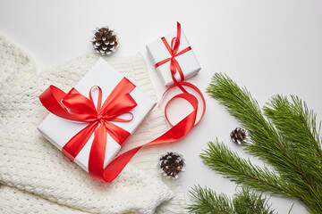 Christmas gift boxes with red ribbon and knitted sweater with green pine tree branch and cones on white