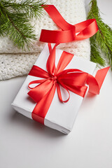 Christmas gift box with red ribbon and knitted sweater with green pine tree branches on white