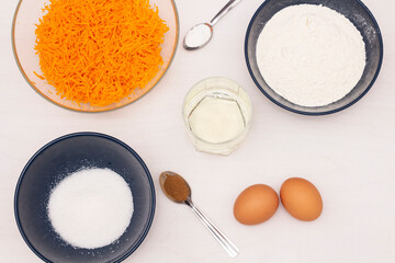 Ingredients for making muffins: grated carrots, flour, sugar, eggs, vegetable oil, cinnamon, baking powder