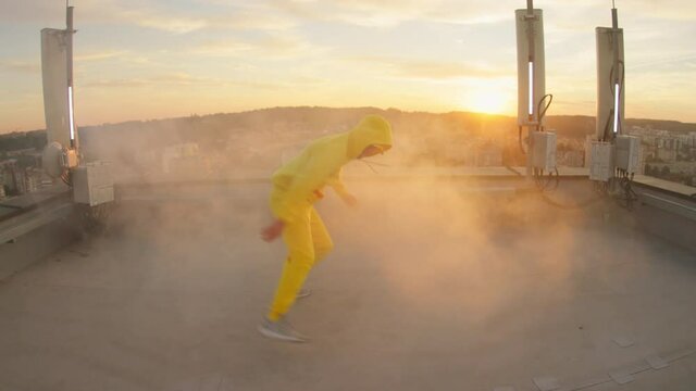 Charismatic active young man bboy dancing hip hop choreography moves and breakdance on the building rooftop. City sunset. Stylish performance.