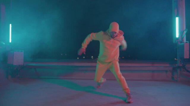 Young handsome hiphop dancer performing freestyle stylish choreography breakdance moves on rooftop stage. Smoke and neon lighting. Night performance.