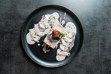 Causa Limeña with olive octopus, on a black plate.
