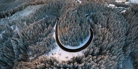 Aerial view of winter landscape with snow covered mountain hills and winding forest road in morning.