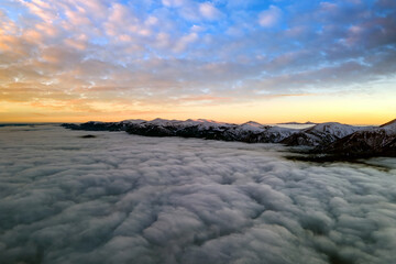 Aerial view of vibrant sunrise over white dense clouds with distant dark mountains on horizon.