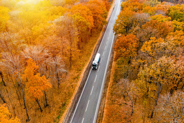 Cargo delivery. white truck with drives on an asphalt road through the autumn forest. cargo transportation. Sunset. Drone photo  aerial view