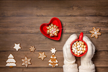 Cozy cup of hot chocolate in a red mug held by mittens with christmas cookies.