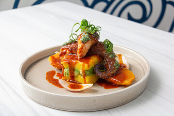 Causa stuffed with tar and avocado, with slices of octopus bathed in sauce.
